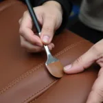 Applying liquid leather filler to repair a burn on a car seat