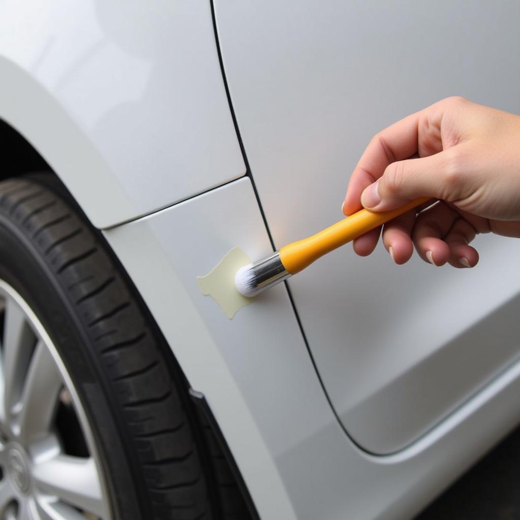 Applying touch-up paint to a car's paint chip using a fine-tipped brush.