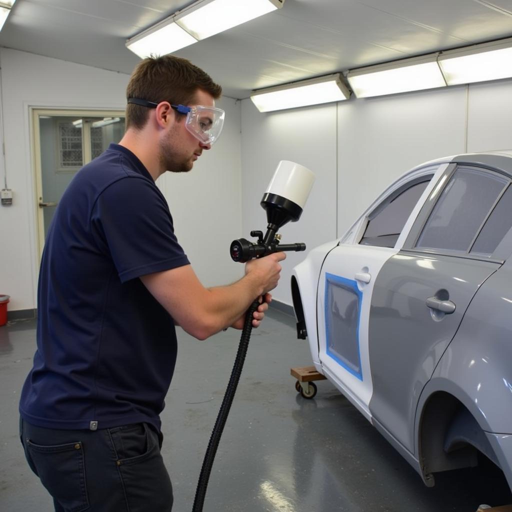 Apprentice applying paint to a car body using a spray gun in a Fareham bodyshop