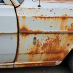 Close-up image of rust damage on a car body panel, showing the different stages of corrosion.