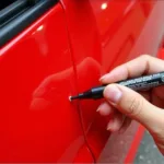 Applying a car paint repair pen to a small scratch on a car door.