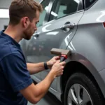 Dent Repair Dracut MA: Close-up of a technician repairing a dent on a car door using specialized tools.