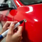 Close-up view of a person repairing chipped car paint on a red car using a touch-up paint pen.